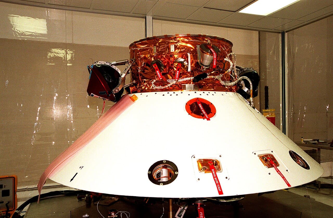 The Mars Polar Lander stack at Kennedy Space Center in November 1998, its white backshell below and the copper-blanketed cruise stage above; the two Deep Space 2 probes are the dark units mounted on either side of the cruise stage.