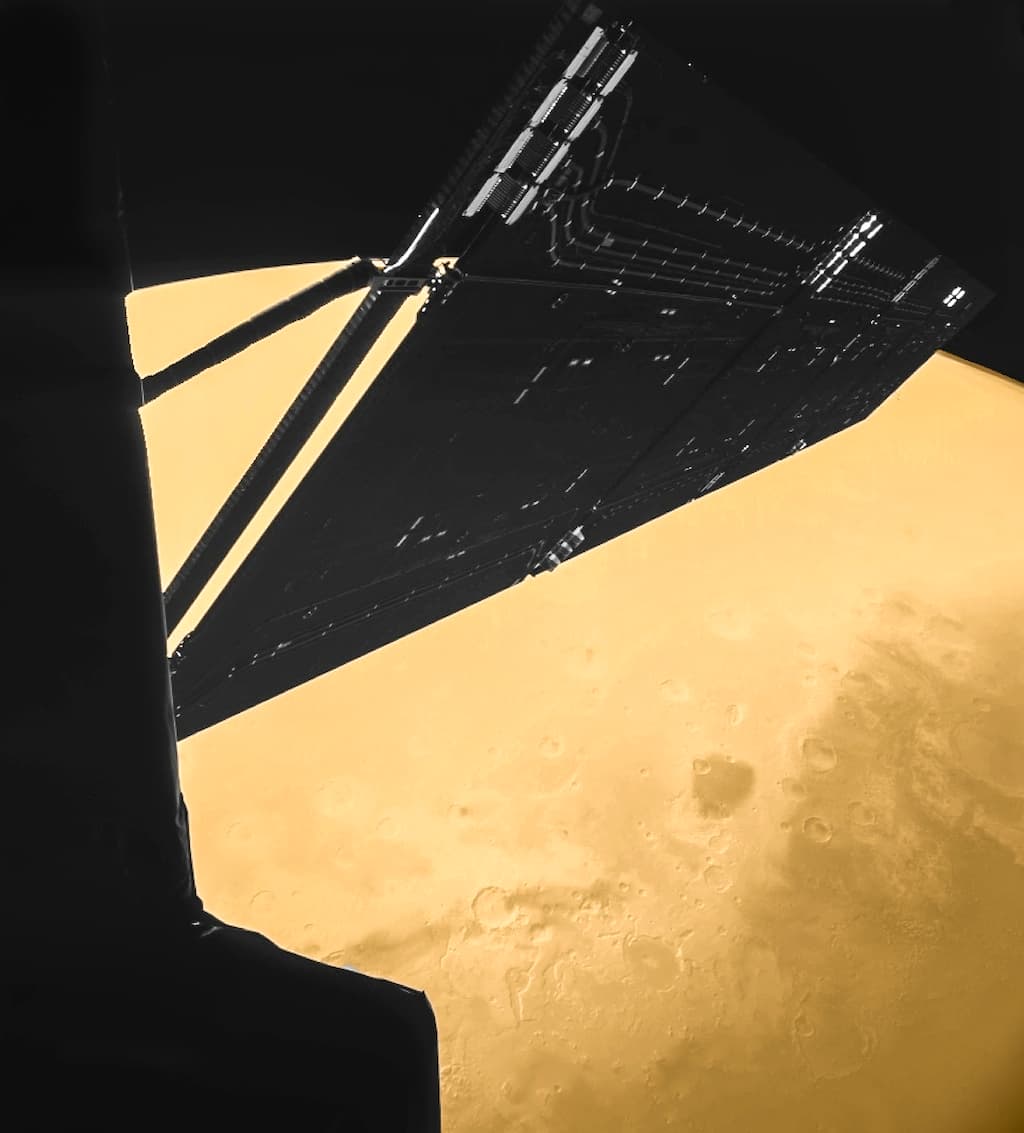 Rosetta photographed by the CIVA camera on its own Philae lander four minutes before closest approach on 25 February 2007, from about 1,000 km, showing one of the 14 m solar wings and part of the spacecraft body against the northern hemisphere of Mars around Mawrth Vallis. ESA's caption states that the frame was taken in black and white, that representative colour was added to the Martian surface for the 2007 release, and that the colours were slightly enhanced again for this 2014 version.