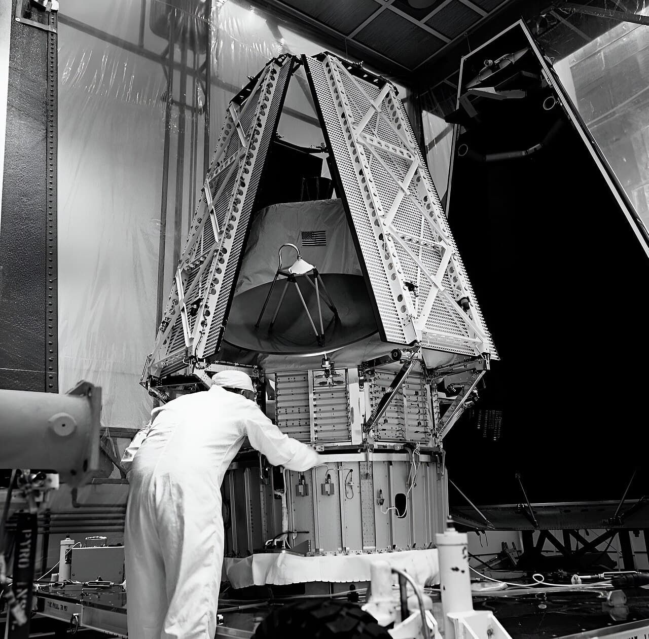 A technician in a clean-room suit works at the base of the spacecraft NASA's caption calls Mariner I, standing inside the opened white panels of its protective enclosure at Kennedy Space Center in May 1971, before encapsulation, with the high-gain dish and the folded octagonal bus visible above him. It was designated Mariner 9 after the Atlas-Centaur launch of 30 May 1971.