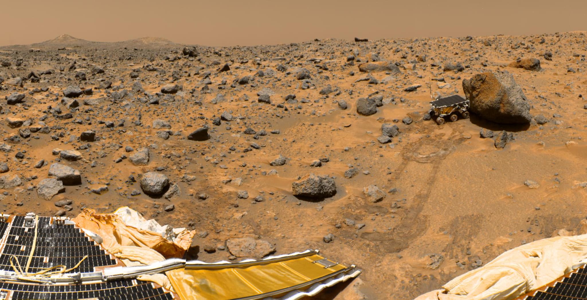A section of the geometrically improved, colour enhanced version of the Gallery Pan, taken by the Imager for Mars Pathfinder over sols 8, 9 and 10, showing Sojourner at the boulder Yogi with the lander's solar panel and deflated airbags in the foreground.