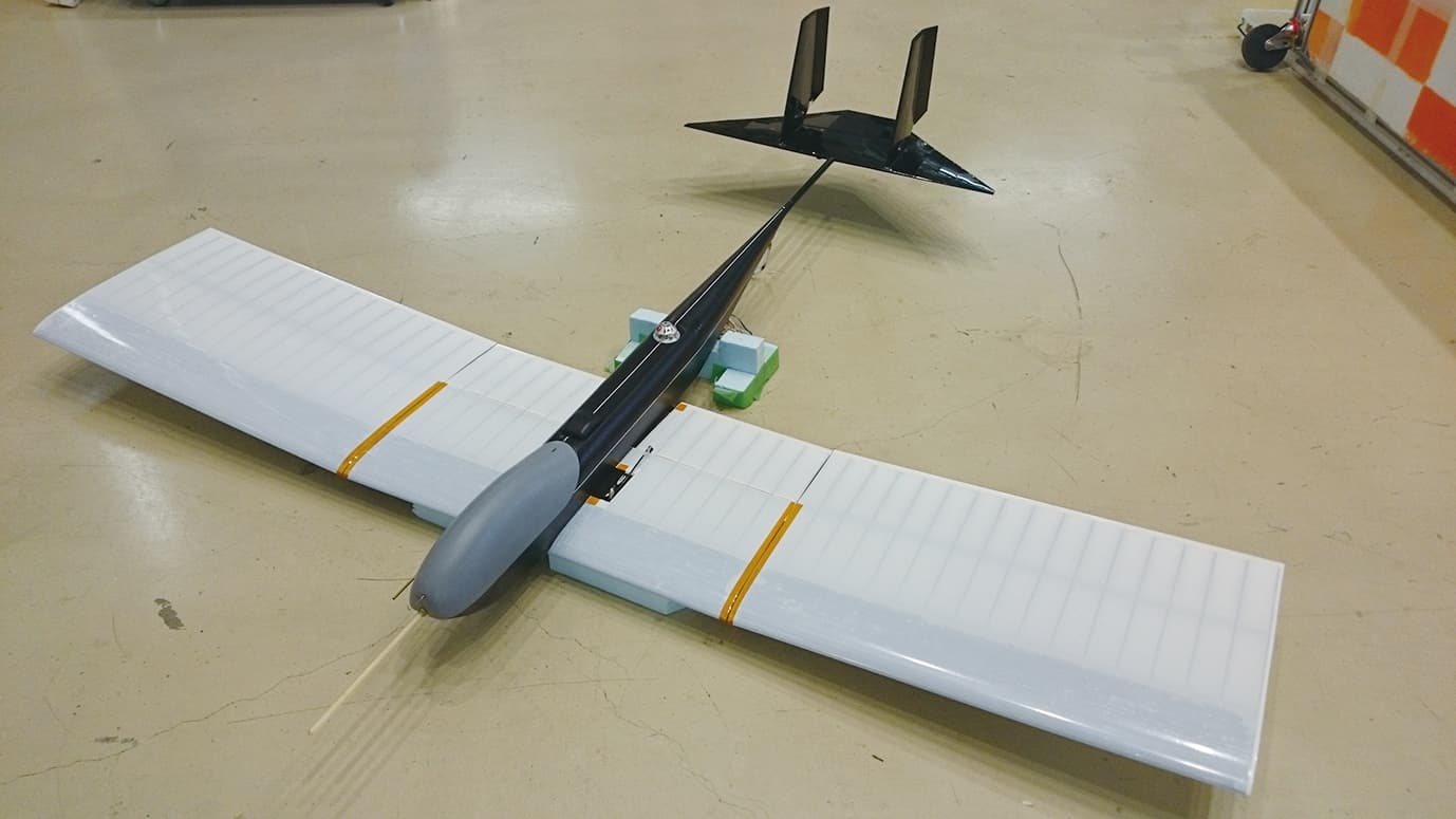 The first Mars exploration aircraft airframe standing on a hangar floor: a straight high aspect ratio wing in taped panels resting on foam blocks, a slim black carbon fibre fuselage pod, a boom running back to a tailplane with twin fins, and no landing gear. The article's Figure 3 caption names it the first unit of the Mars exploration aircraft, the airframe carried to 36 km by balloon and released nose down.