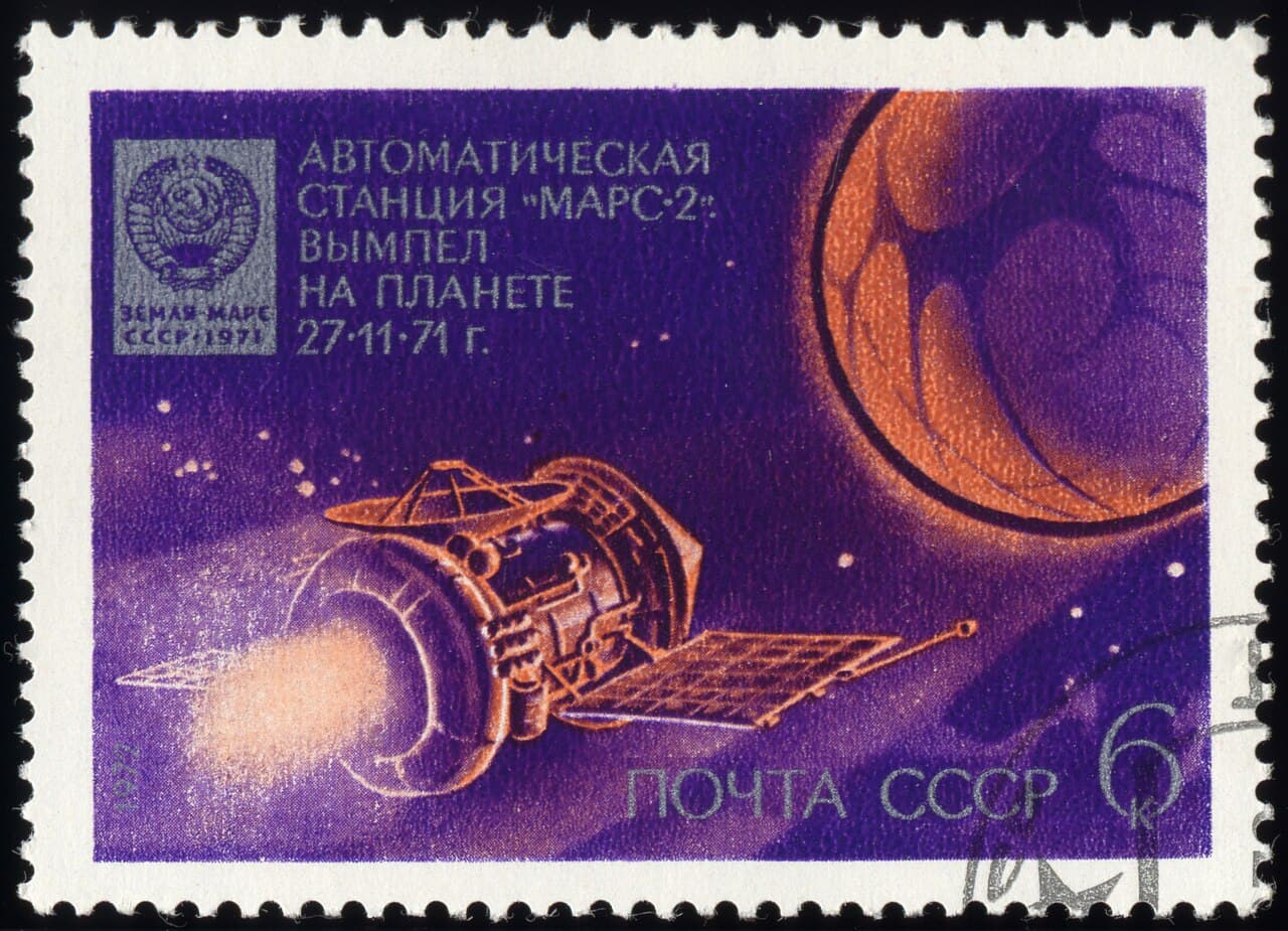 A six kopeck Soviet stamp issued in 1972 and headed Автоматическая станция «Марс-2»: вымпел на планете 27.11.71 г., showing a painted M-71 station firing its engine beside a crescent Mars, with an inset panel at the upper left depicting the pennant itself: a plate carrying the State Emblem of the USSR and the words ЗЕМЛЯ МАРС СССР 1971.