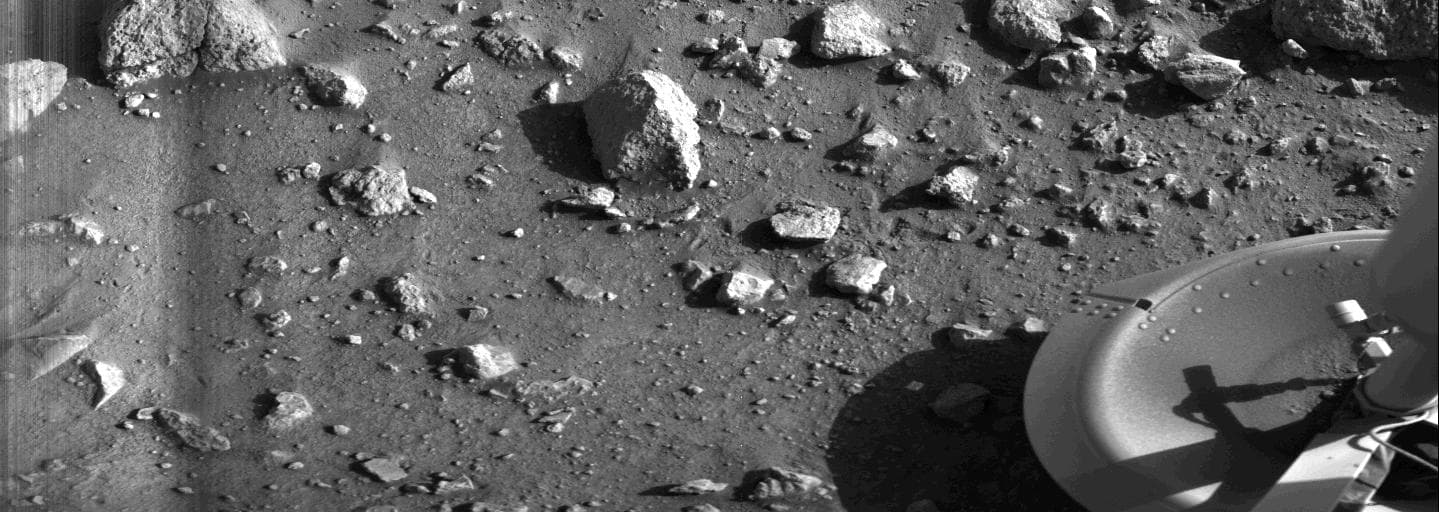 The first photograph ever taken from the surface of Mars, scanned by Viking 1 camera 2 starting about 25 seconds after touchdown on 20 July 1976, showing rocks, fine soil and one of the lander's footpads at lower right.
