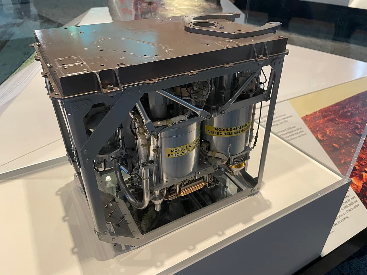 An unflown Viking lander biology instrument on museum display, opened so that two of the three experiment modules are visible with their original engineering labels reading MODULE ASSEMBLY PYROLYSIS EXPERIMENT and MODULE ASSEMBLY LABELED RELEASE EXPERIMENT. The photographer records the object as being on display at the Cleveland Museum of Natural History.
