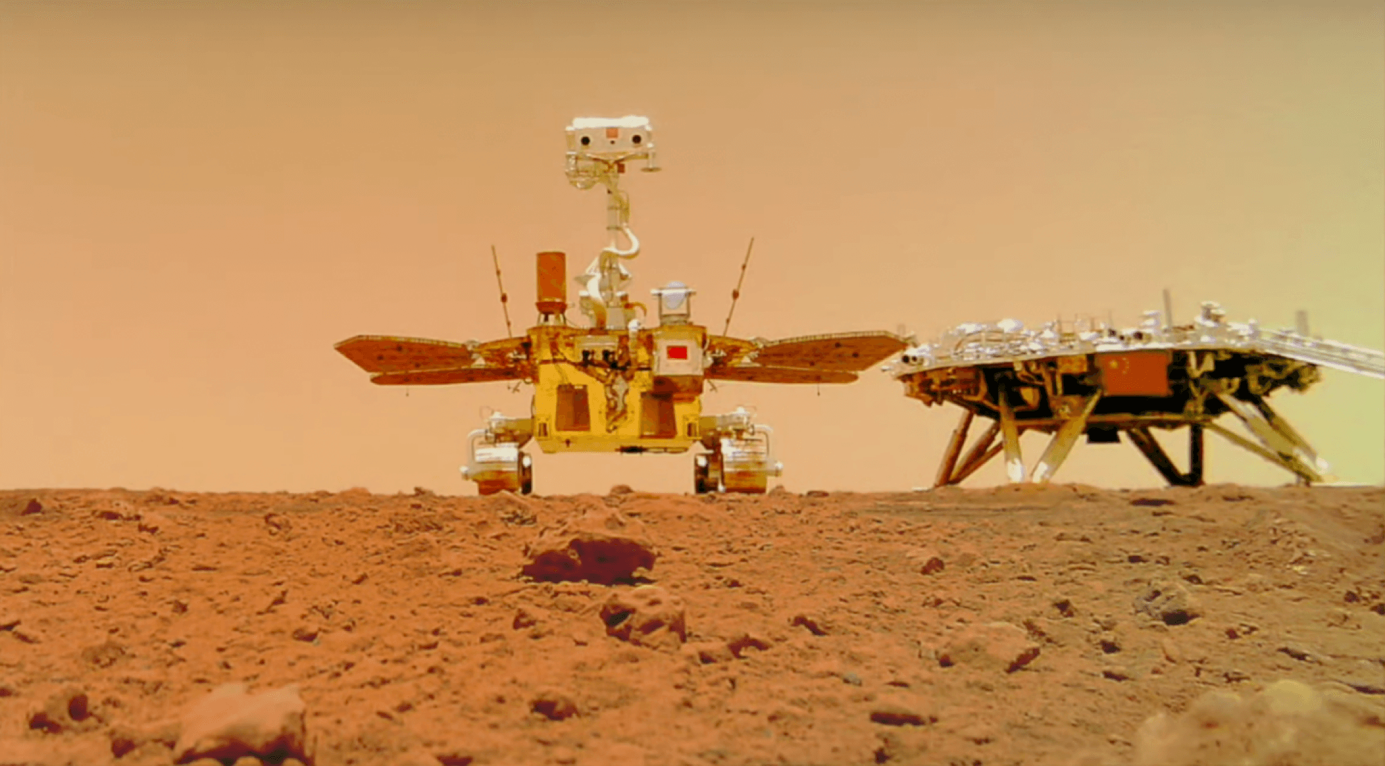 Zhurong and the Tianwen-1 landing platform standing side by side on the surface of southern Utopia Planitia, photographed by a small wireless camera that the rover set down on the ground and then drove away from.