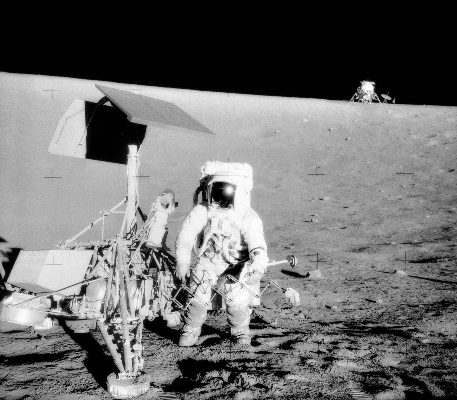 Pete Conrad stands at Surveyor 3 during Apollo 12, the lunar module Intrepid on the horizon behind him