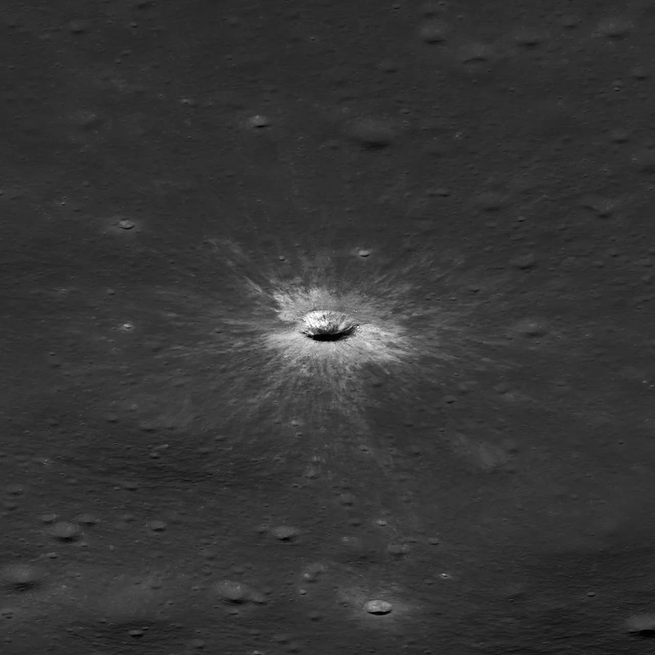 McGetchin crater seen at a slant, a bowl-shaped crater with a bright rim and a pale splash of ejecta on flat grey ground